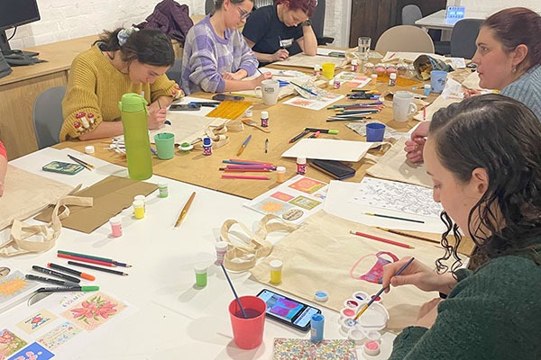 A group of people sat around a table, all creating with pens, paper, brushes and various art materials.